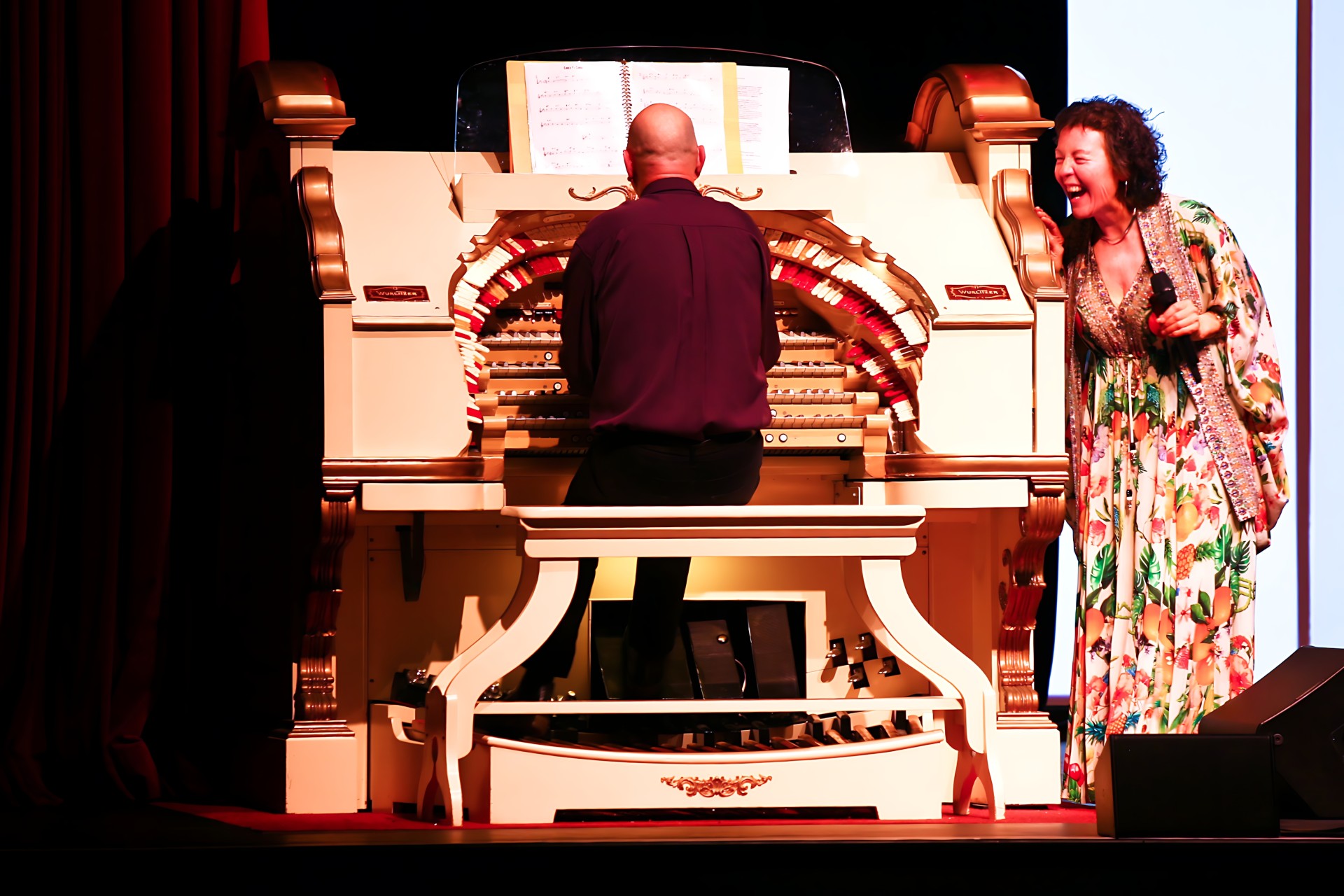 Ruby Page laughing beside Scott Harrison as he plays the Wurlitzer